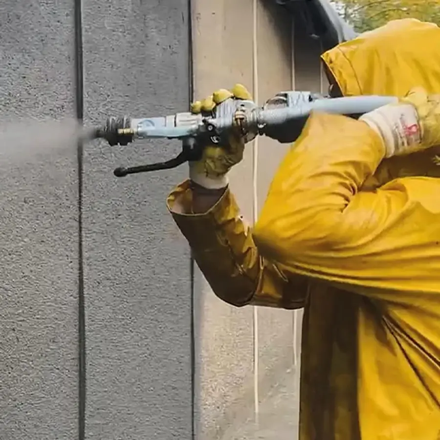 Verarbeiter in Schutzkleidung trägt Mörtel mit der Nassspritzdüse auf eine Betonwand auf